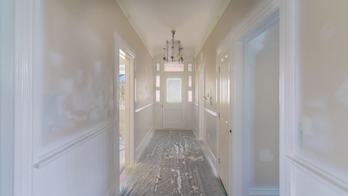 A long villa hallway before painting, with patched and filled walls and drop sheets on the floor