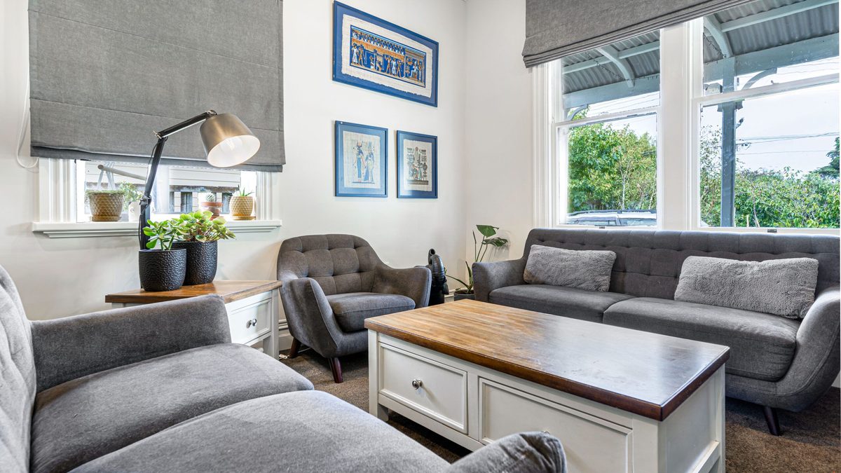 A living room with white walls and window frames, grey sofas, framed blue prints and a timber-topped coffee table