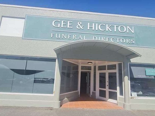 The shopfront of Gee and Hickton Funeral Directors, painted pale green-grey with white window joinery and an arched entrance